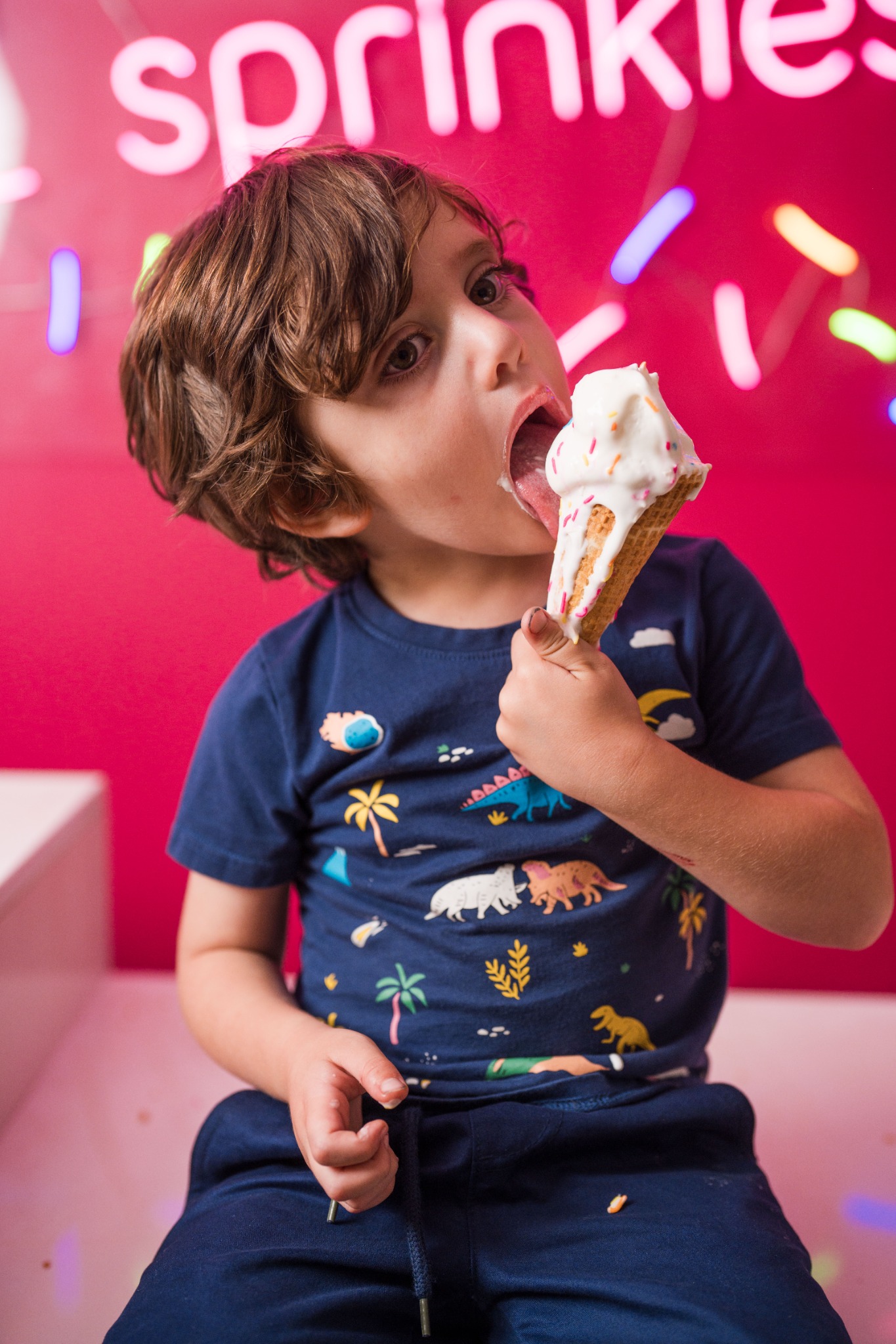 A child enjoying an ice cream in front of a bright pink JoyJozi backdrop