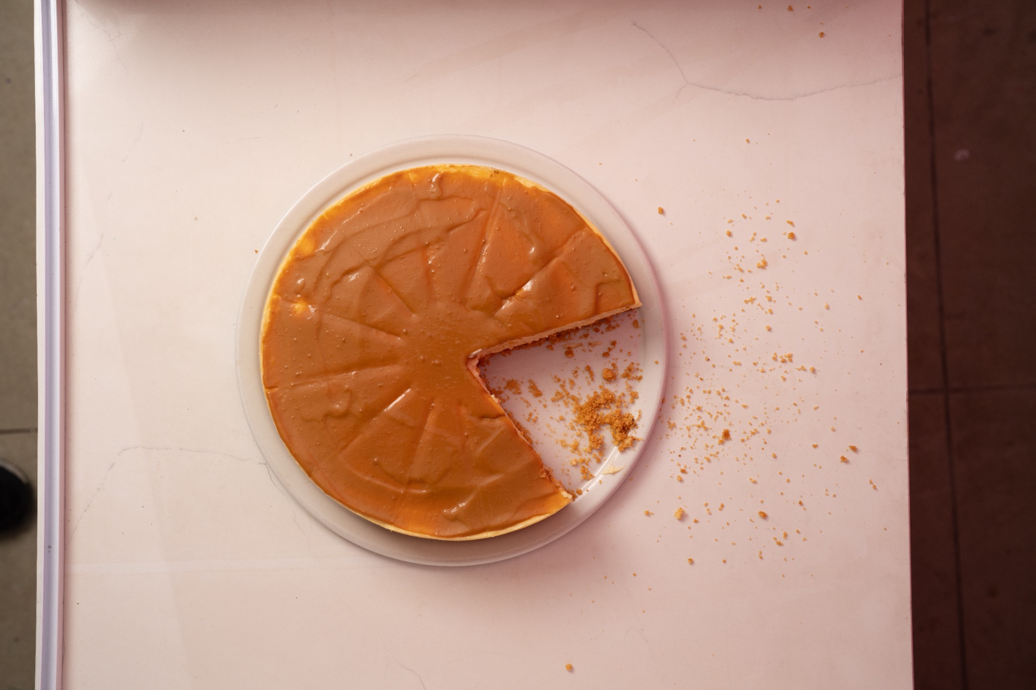 A whole cheesecake with one slice removed on a pale tabletop