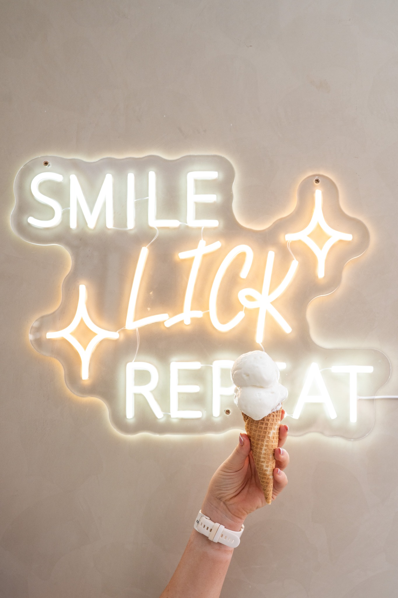 A vanilla ice cream cone held up in front of a Smile Lick Repeat sign