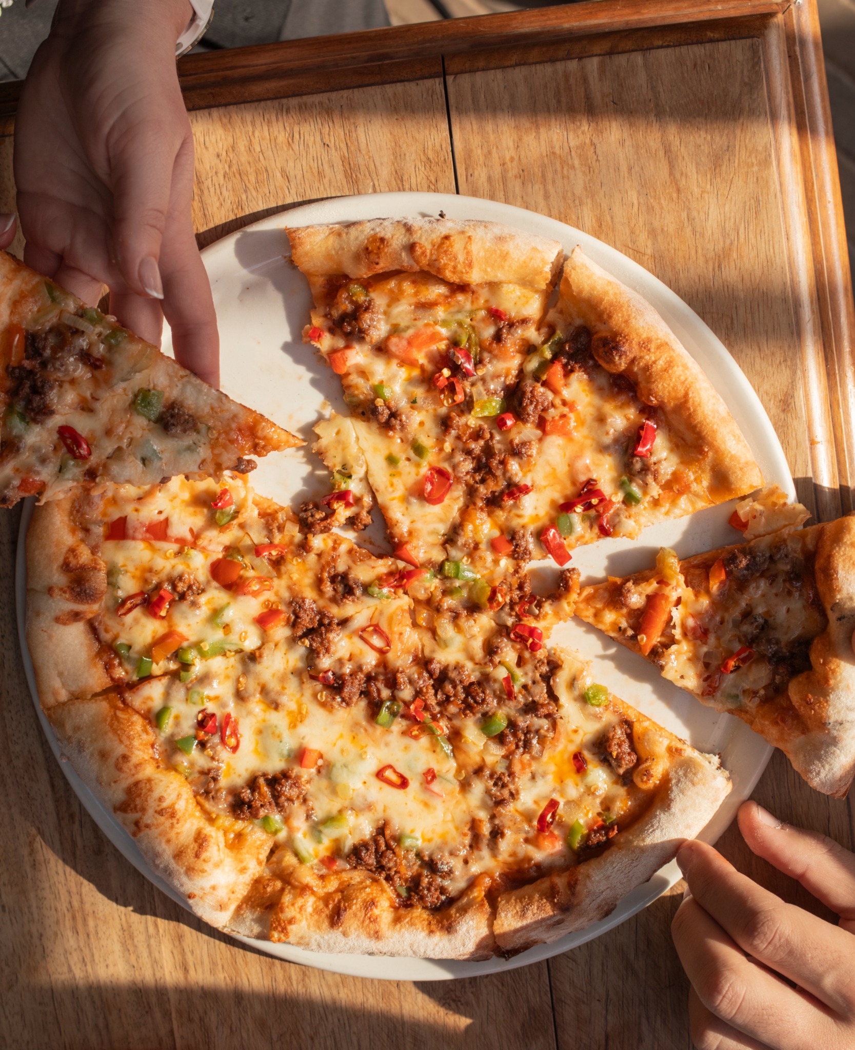 A pizza on a table with slices being lifted