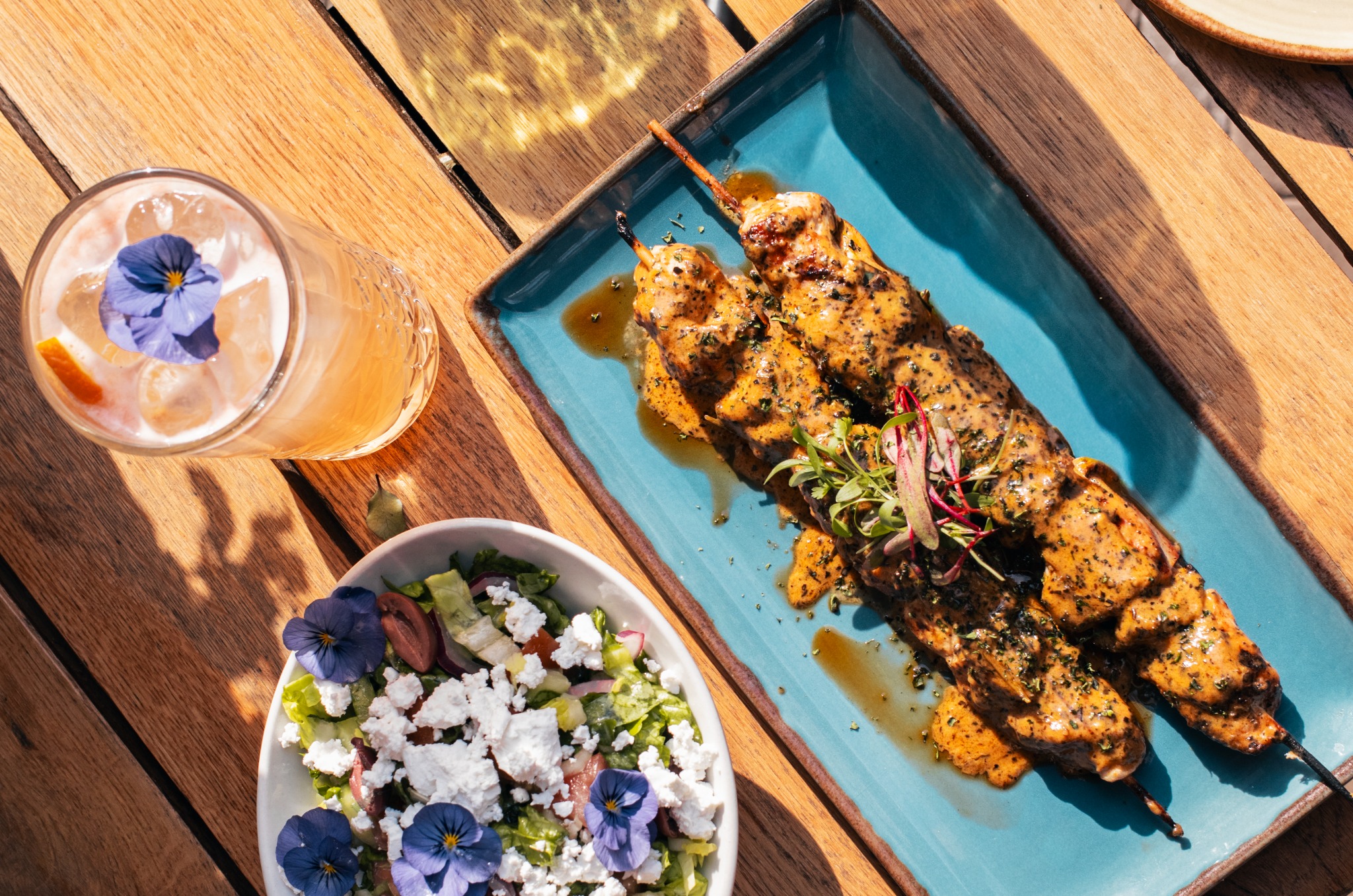 Chicken skewers with a salad and drink on a wooden table